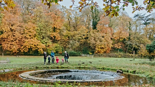 The cup and saucer waterfall in Erddig, Wales, where water flows down into a circular aperture, while a family watches with autumn trees in the background